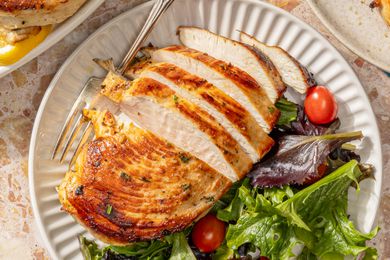 half sliced baked chicken breast on a plate with a side of mixed greens and cherry tomatoes