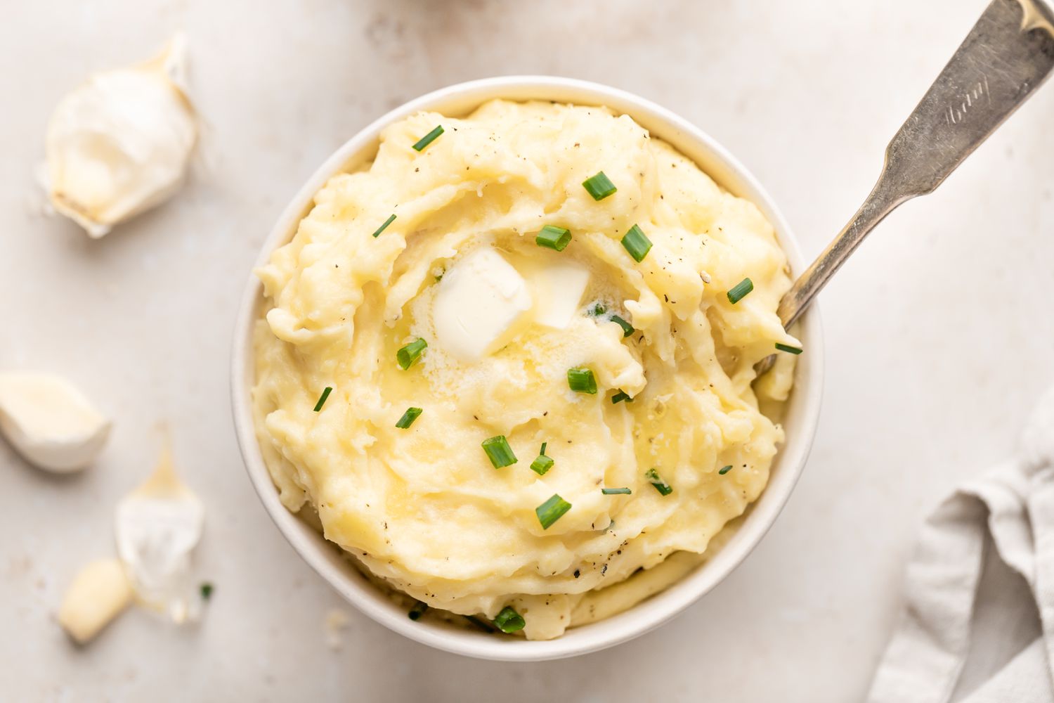 Overhead view of garlic potatoes in a white bowl with garlic cloves around it.