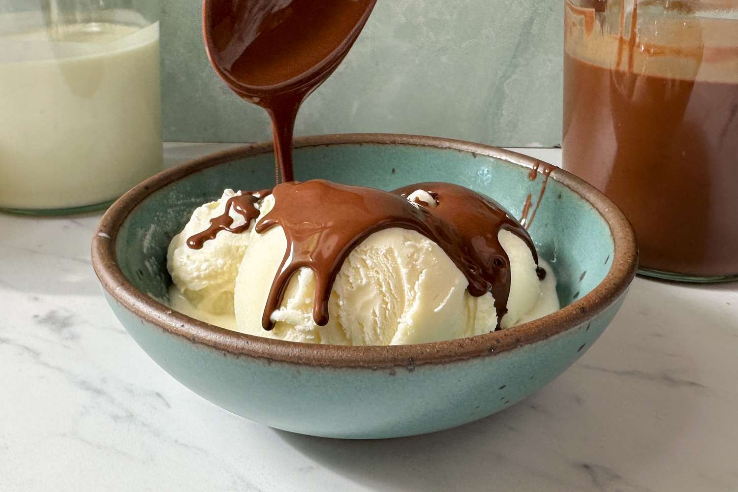 Vanilla ice cream in a bowl being topped with melted chocolate sauce