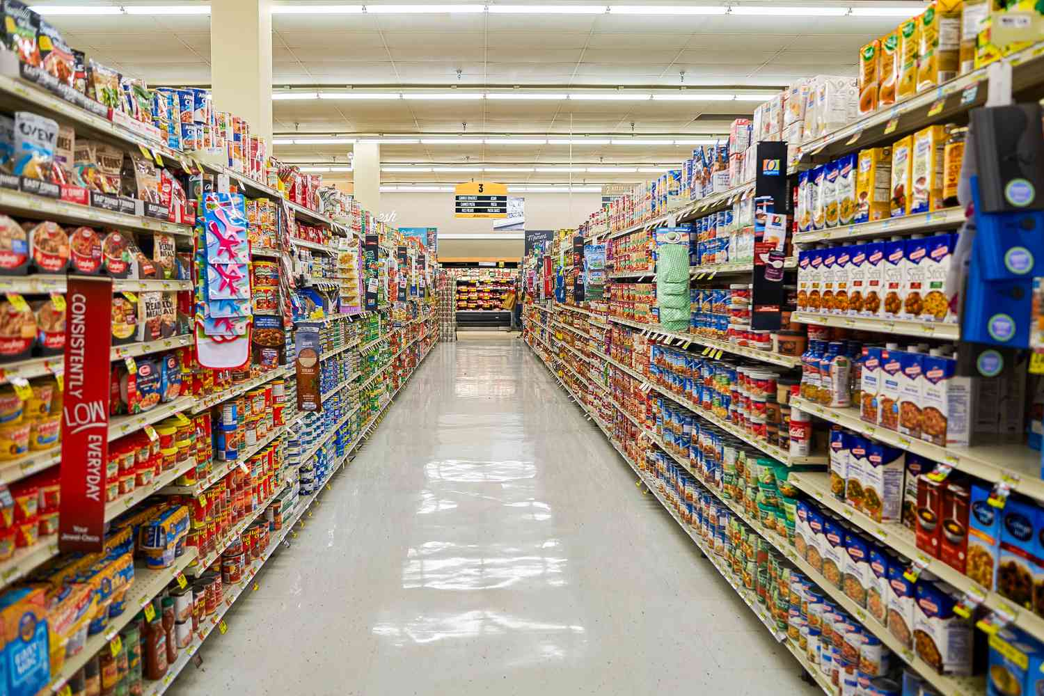 View looking down a grocery store aisle with canned tomatoes, pasta and sauce, rice and beans, soups and asian items on the shelves