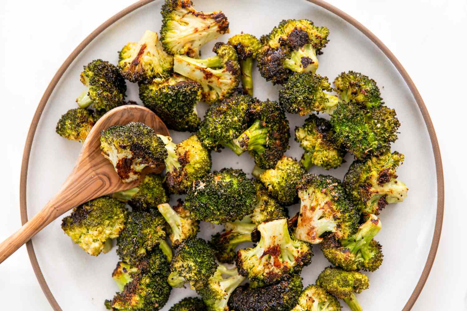 Roasted broccoli on a plate with a wooden spoon