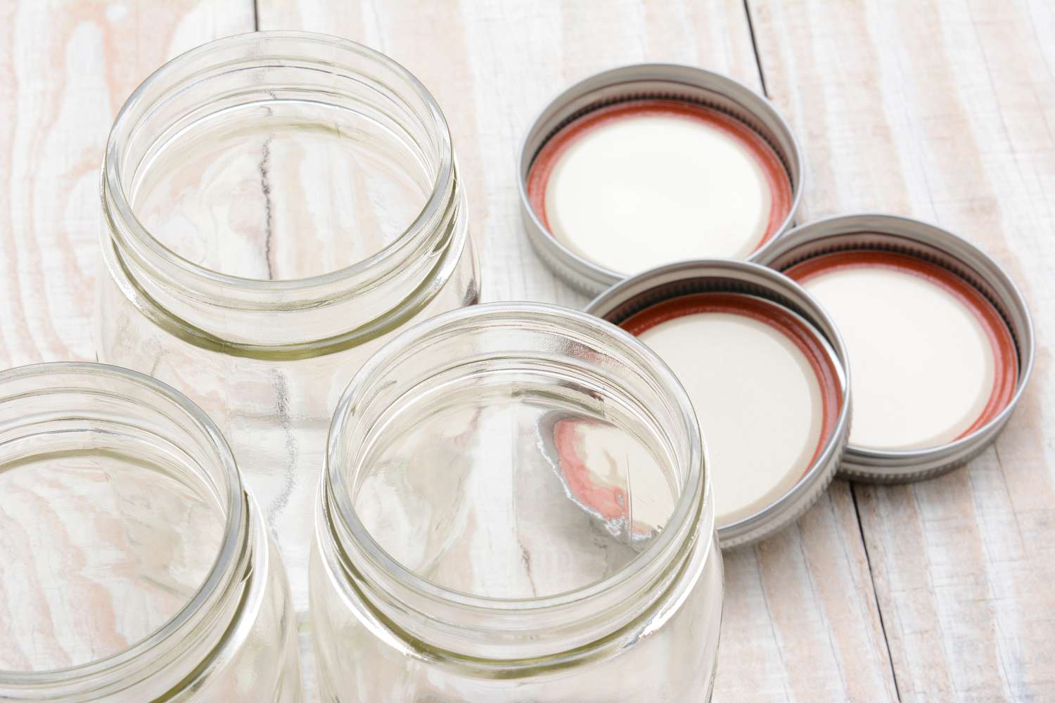 Three open canning jars and lids laying flat on a wooden surface