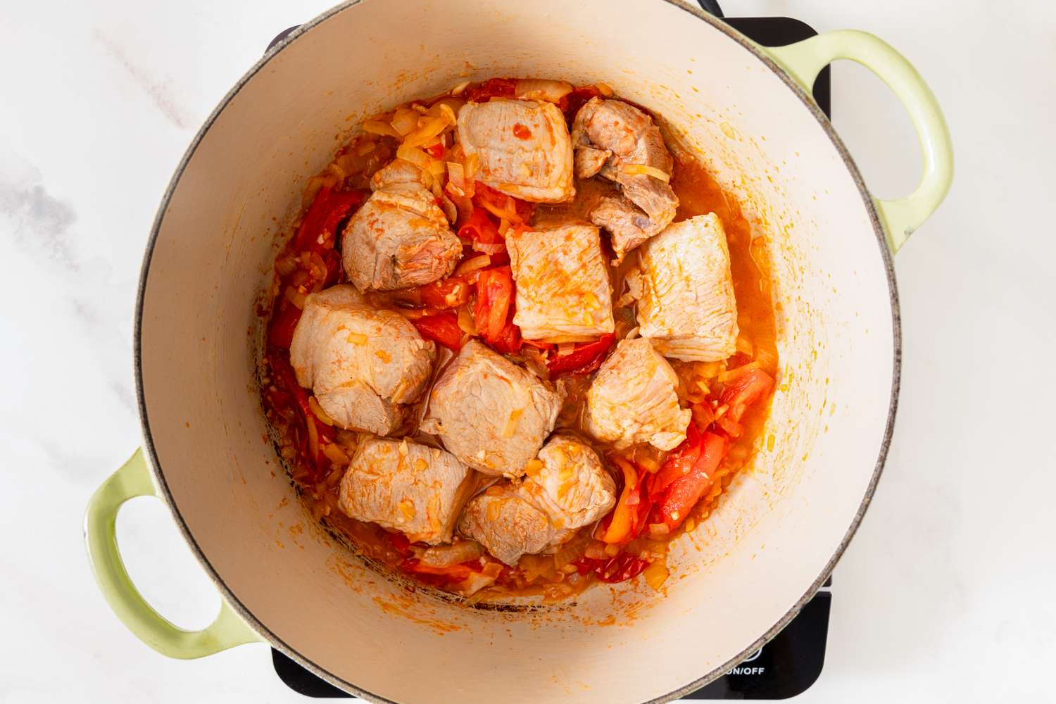 A simmering pot containing pork and tomatoes in a seasoned broth