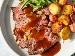 Sliced roast beef with gravy accompanied by roasted potatoes and greens on a plate