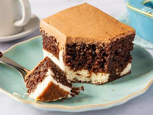 A piece of layered chocolate cake with cream filling and chocolate frosting on a plate, with a fork beside it