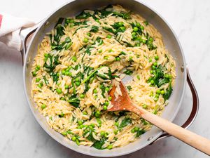 Orzo dish with greens and a wooden spoon in a pan