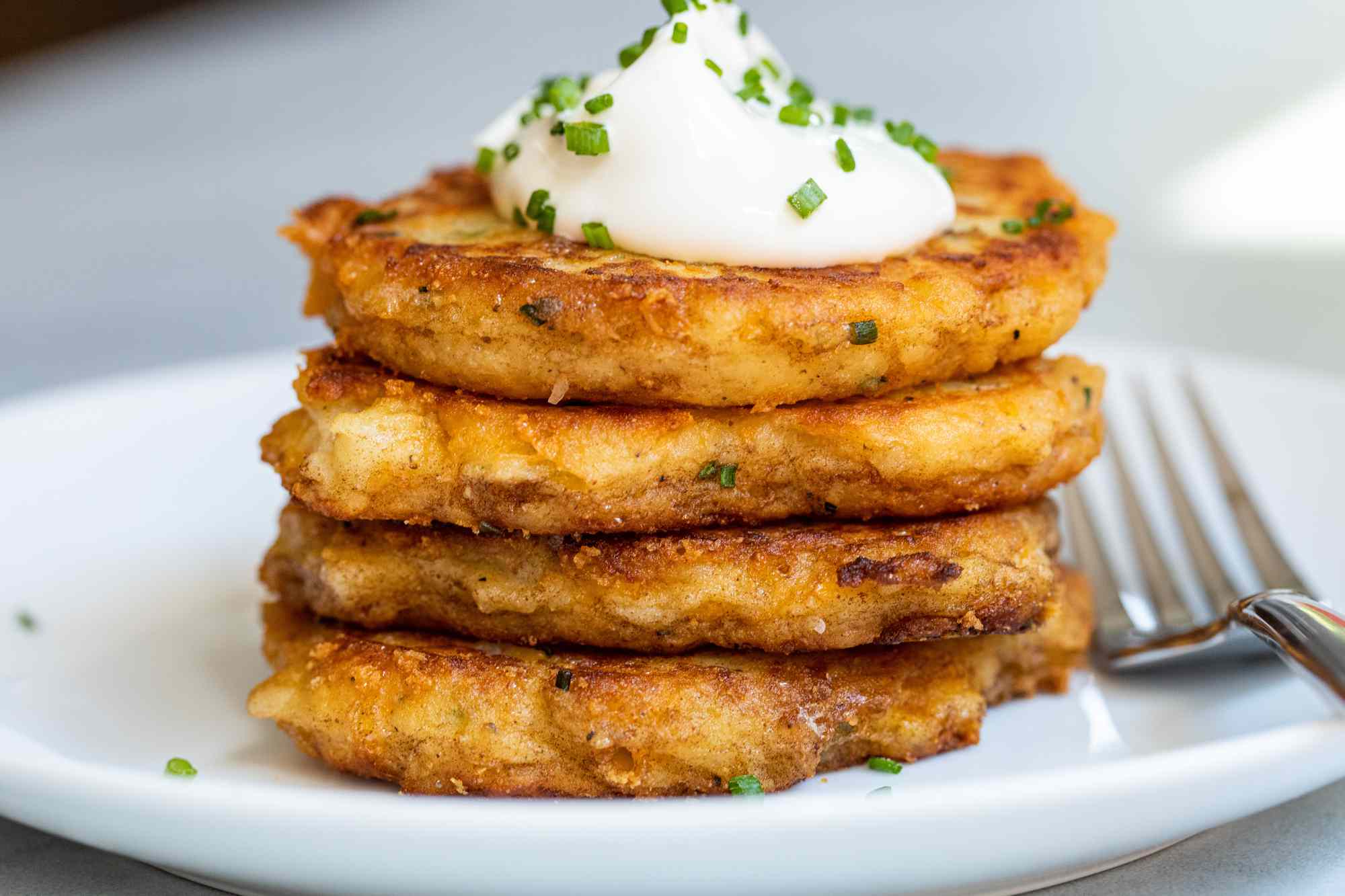 Leftover mashed potato pancakes stacked on a plate and topped with sour cream and chives.