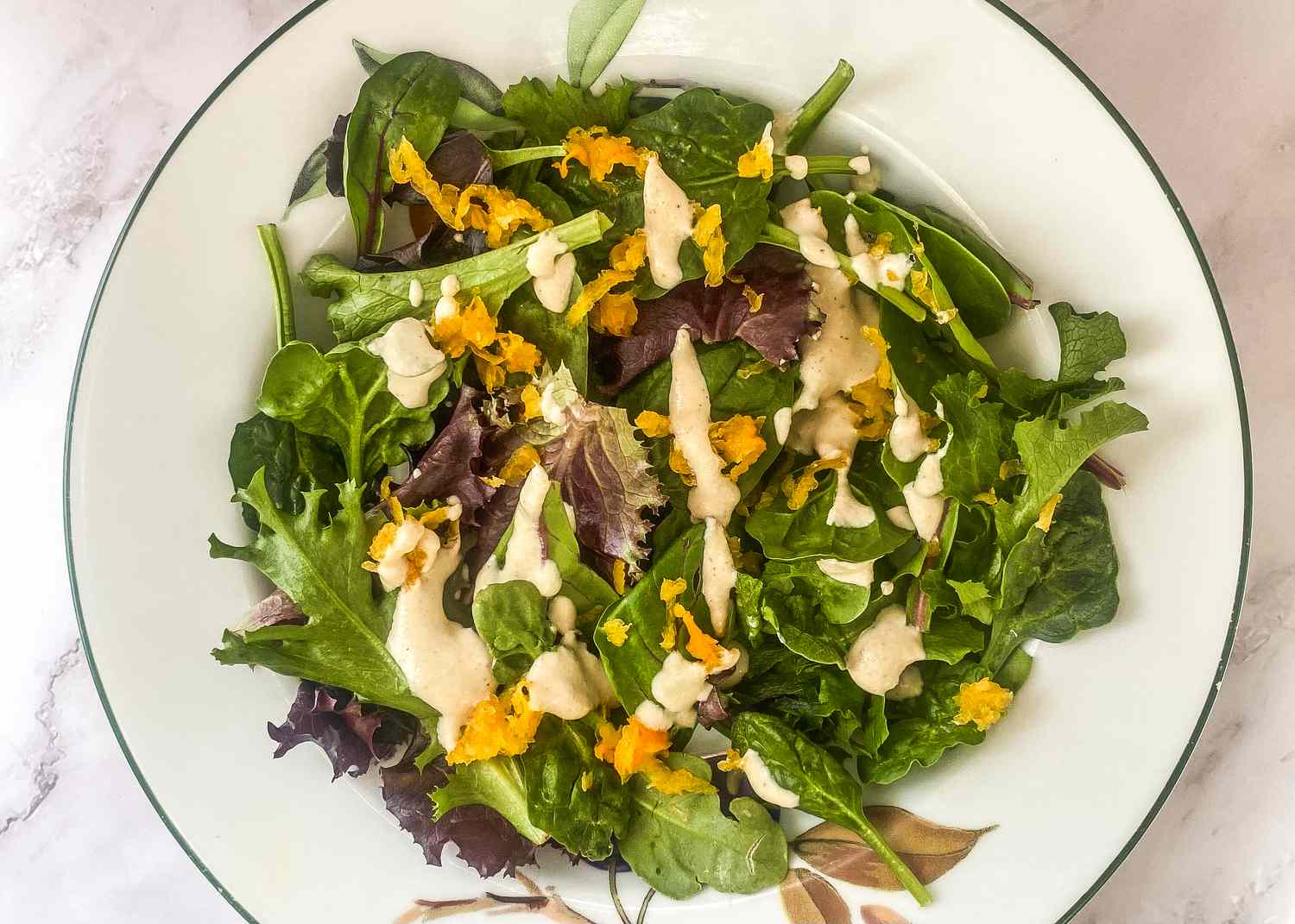 Fresh salad with mixed greens, drizzled cashew dressing, and orange garnish, plated on a patterned dish.