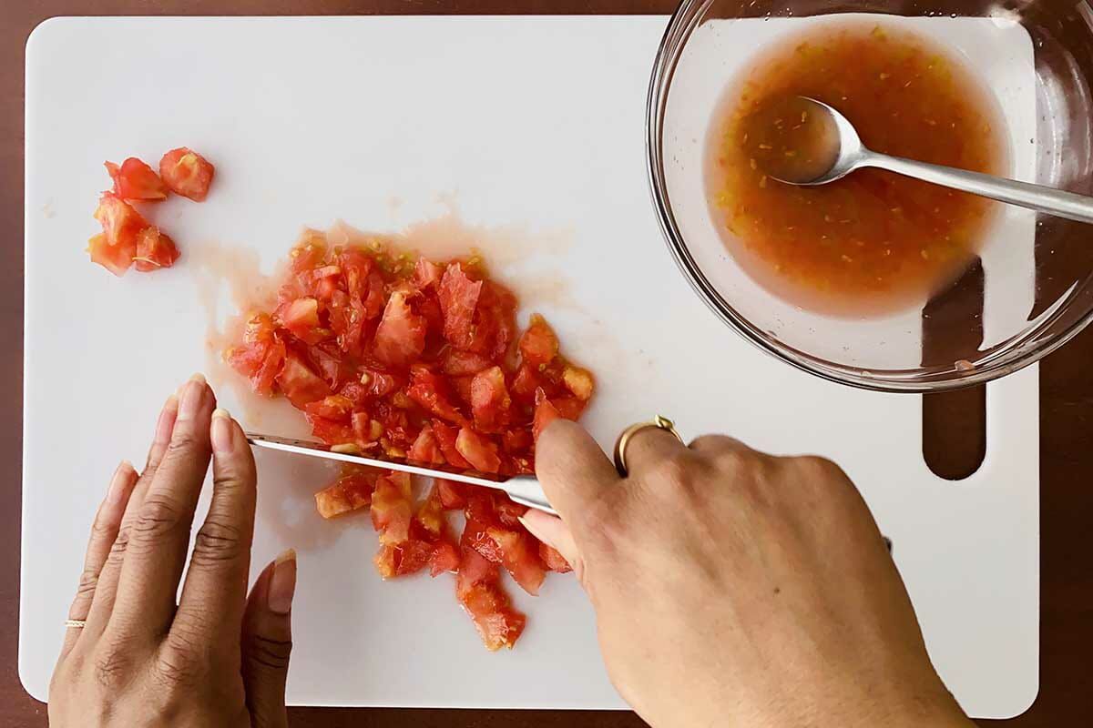 The core and seeds of a tomato are chopped on a cutting board to make easy baked stuffed tomatoes.