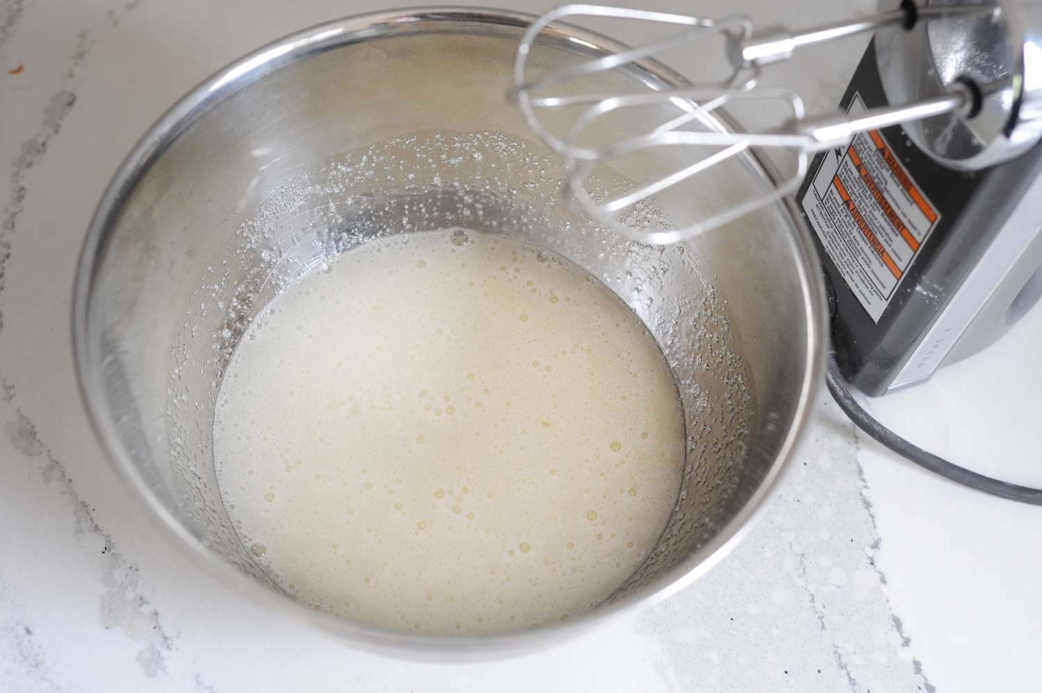 A metal bowl and hand held mixer making Strawberry Seven-Minute Frosting.