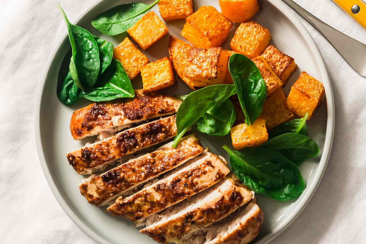 Overhead view of a plate roasted chicken breast, pumpkin and spinach on a light background