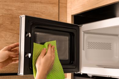 A person cleaning a microwave interior with a cloth