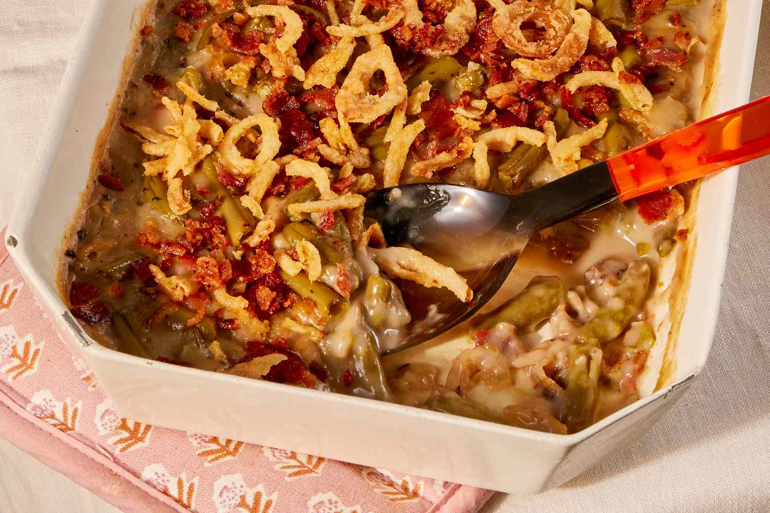 Angled view of a beige casserole dish with green bean casserole along with a serving spoon