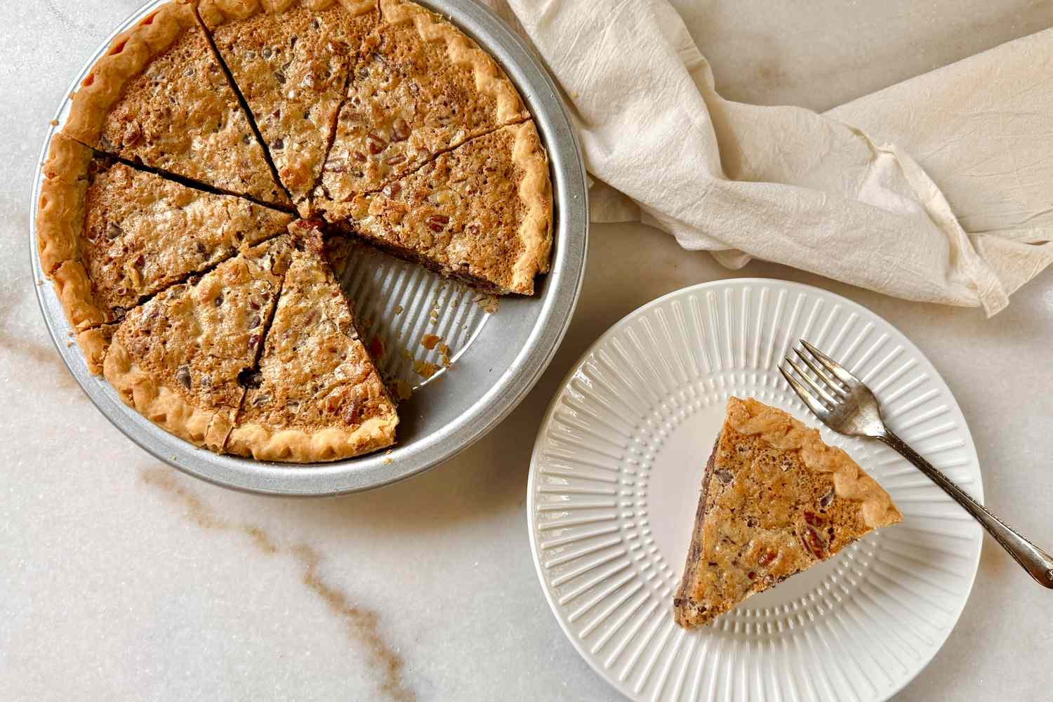 A pecan pie sliced in a pan with one slice served on a plate with a fork