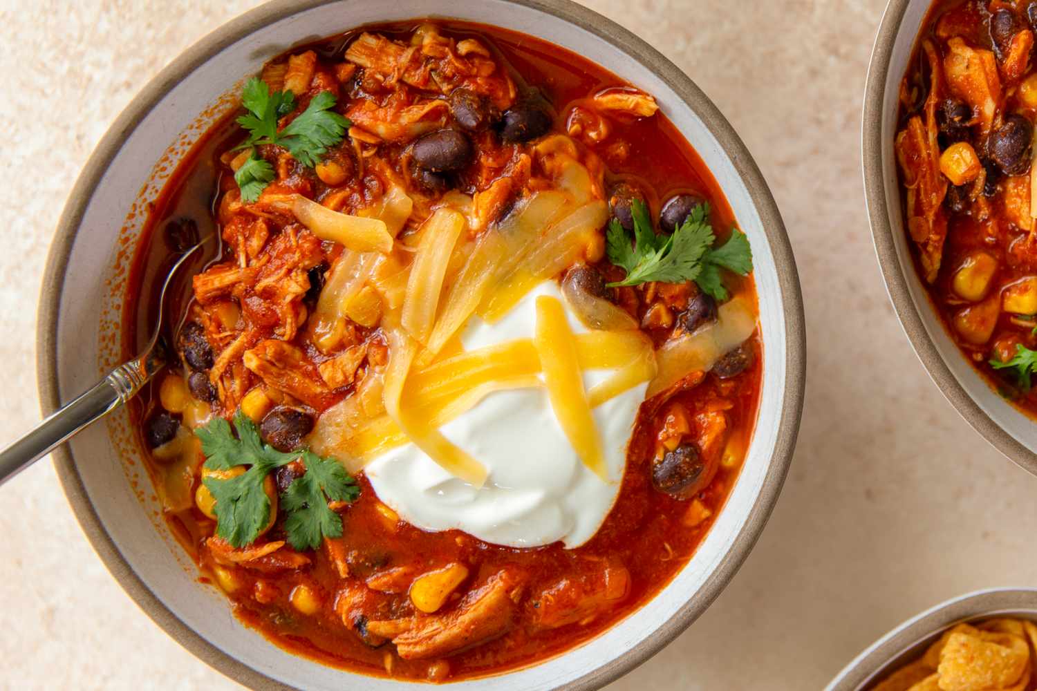 A bowl of chicken enchilada chili topped with sour cream shredded cheese beans and cilantro