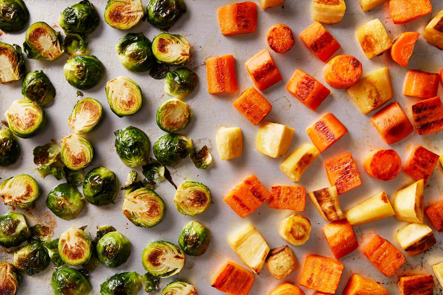 Roasted Brussels sprouts and cubes of root vegetables arranged on a sheet pan