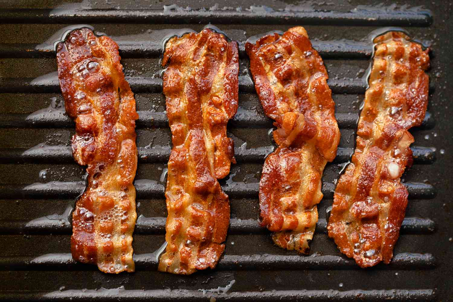 bacon slices cooking on a griddle