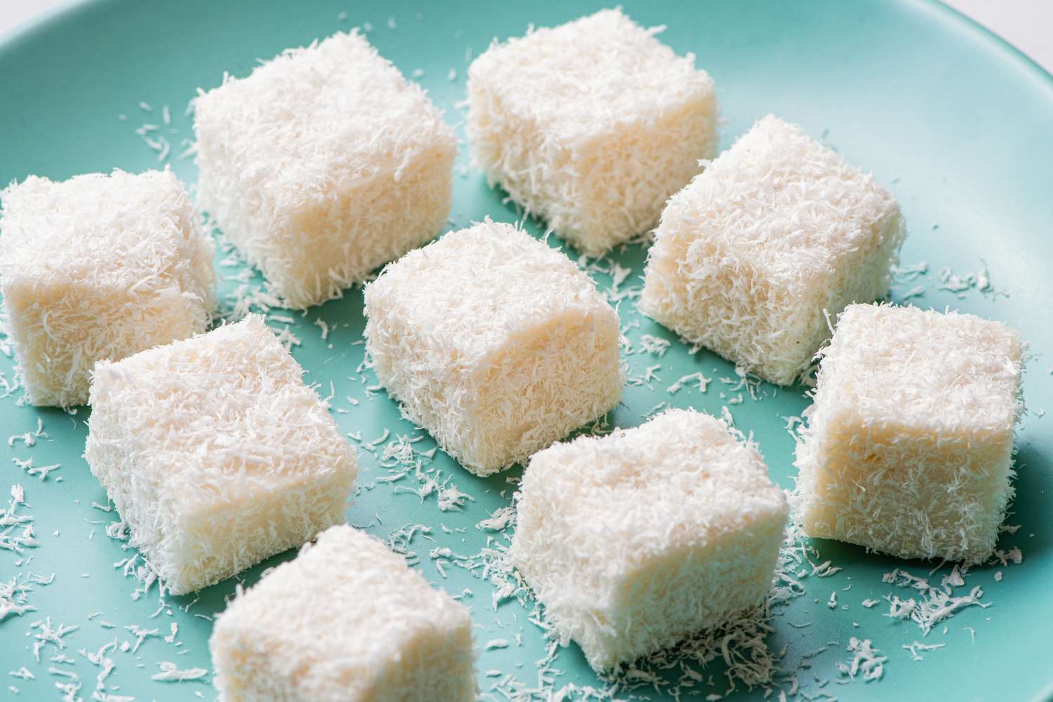 Coconut milk-based dessert squares coated with shredded coconut, arranged on a plate