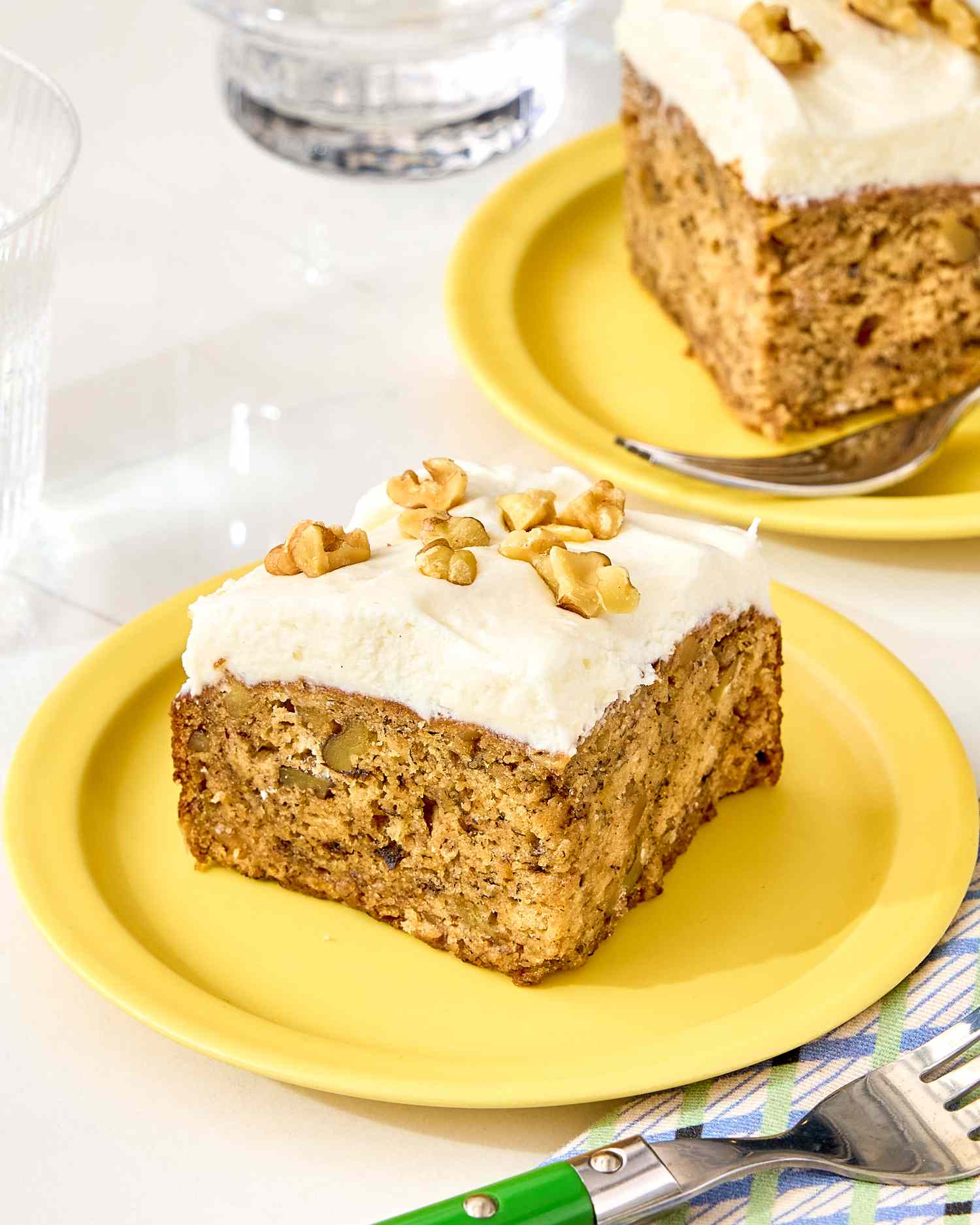 A piece of banana bread cake with frosting and nuts on top served on a yellow plate