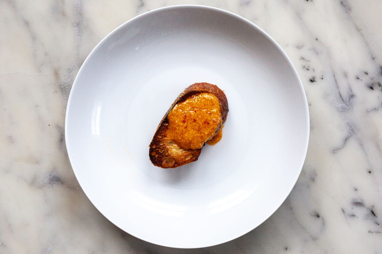 A piece of bread with rouille sauce on a white plate.