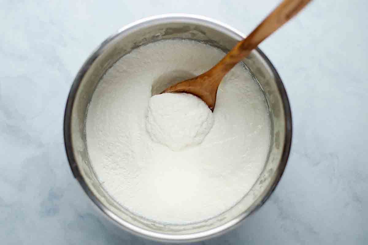 Yogurt resting in a bowl with a wooden spoon collecting a scoop 