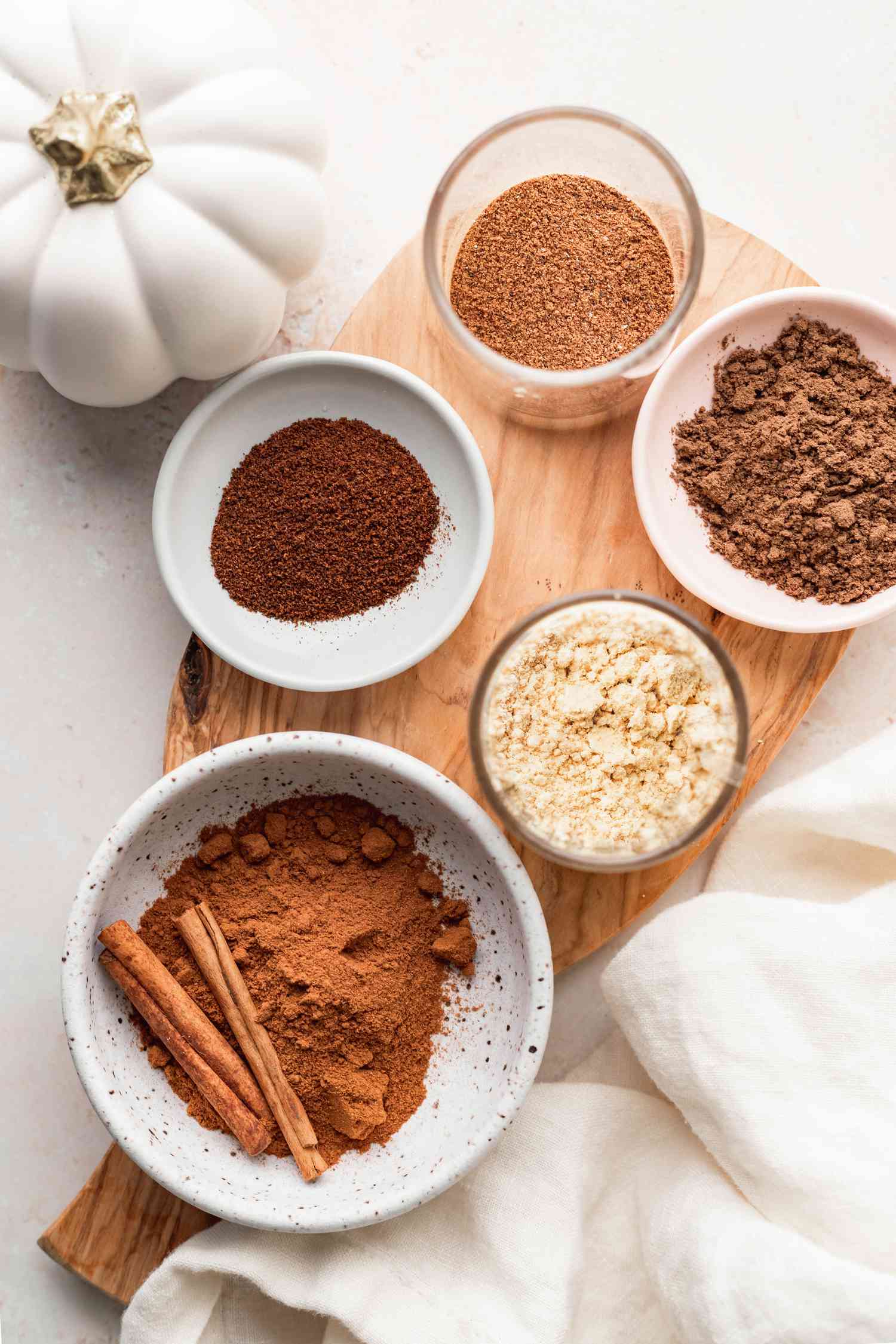 Overhead view of small bowls of individual spices set on a wooden cutting board to show how to make pumpkin pie spice.