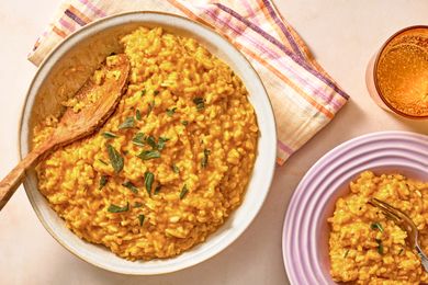 Bowl of pumpkin risotto with herbs and a wooden spoon