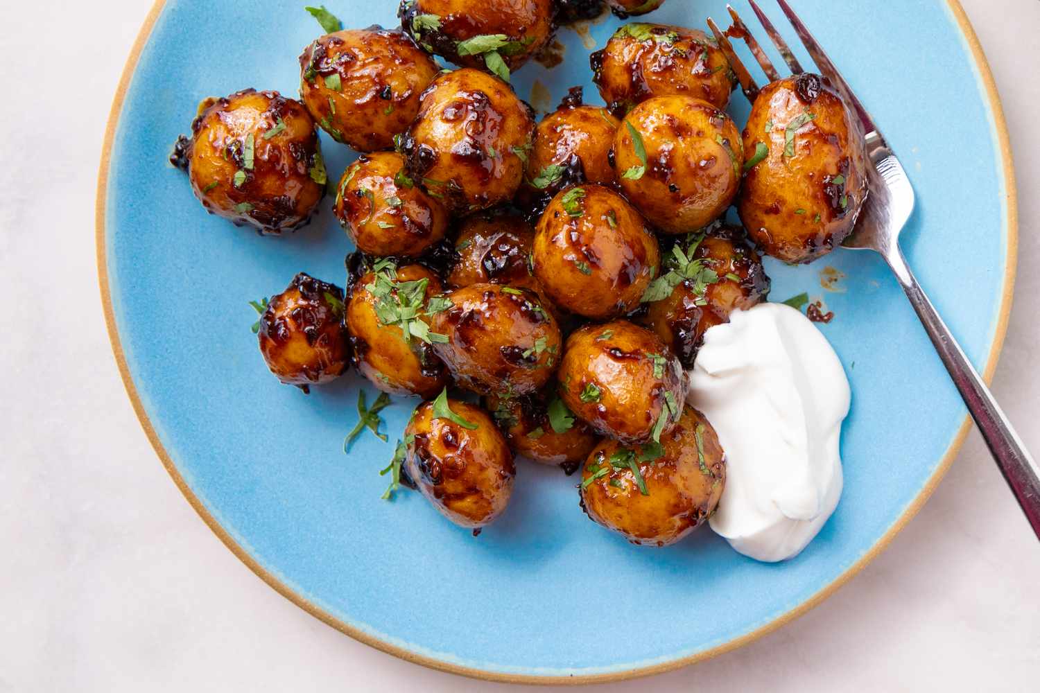 Dish of glazed baby potatoes with herbs served with a side of sour cream on a blue plate