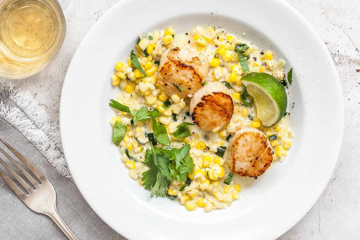 pan seared scallops with creamed corn and lime on a white plate