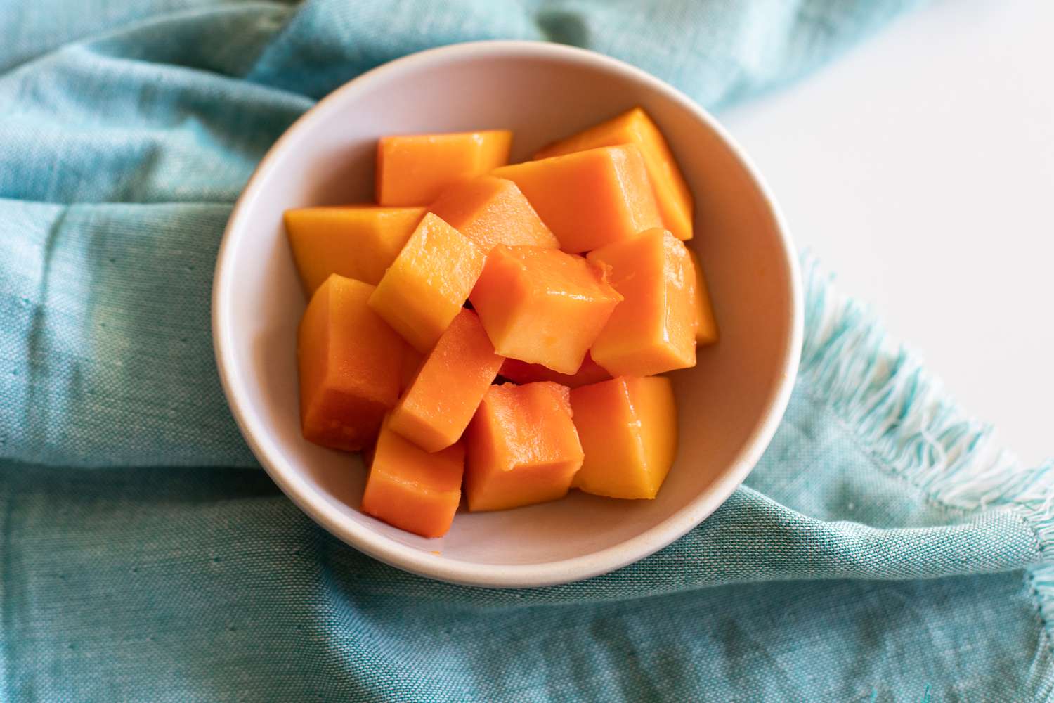 Papaya cubes in a white bowl on a blue napkin