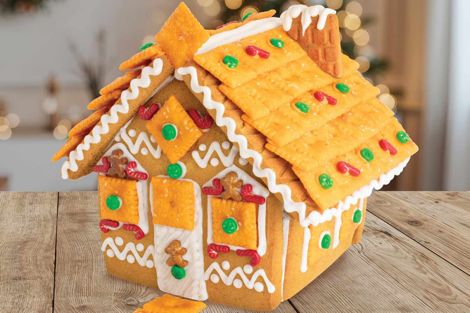 A gingerbread house constructed with crackers and decorated with candies and icing displayed on a wooden table in a festive setting