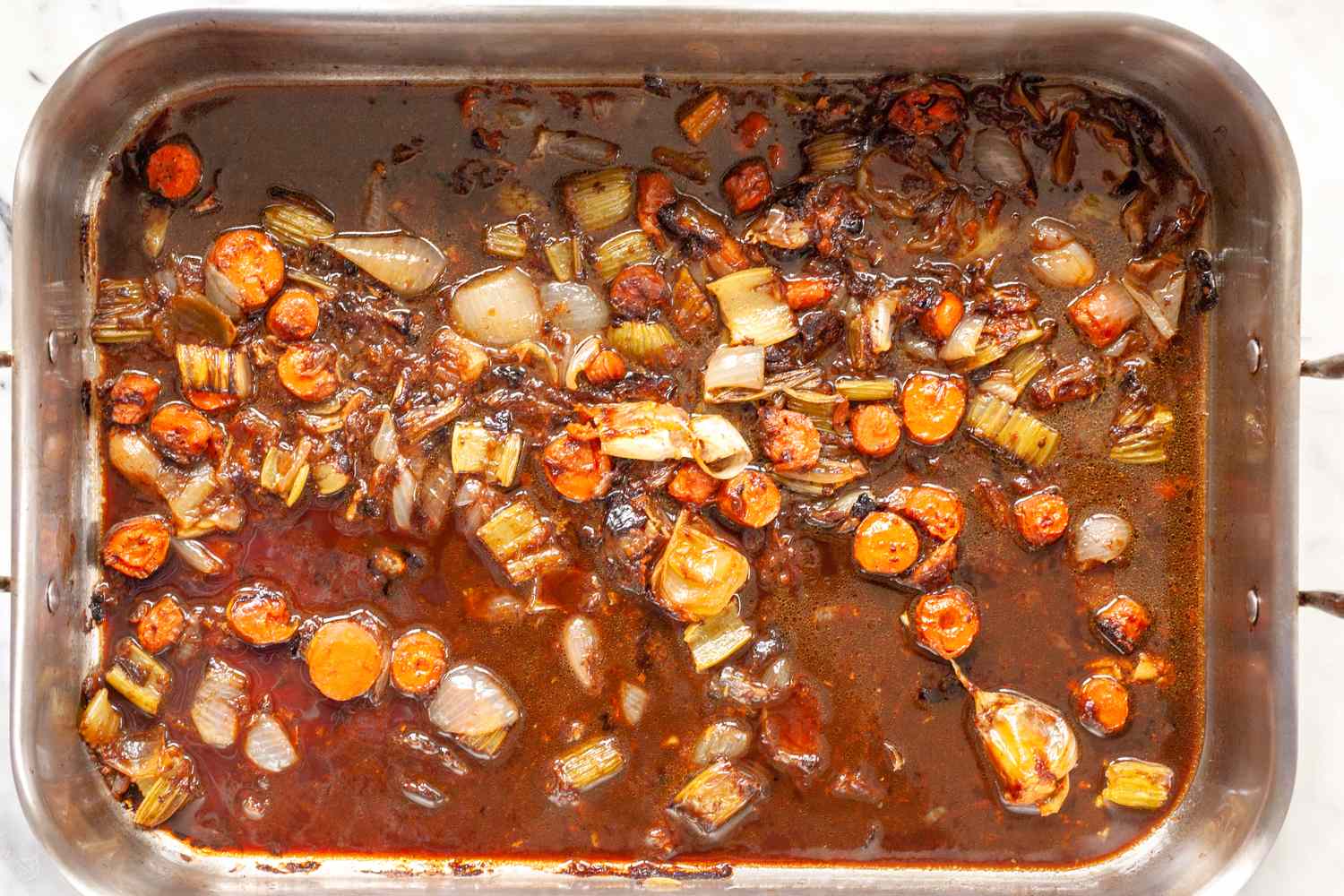Pan of roasted vegetables with liquid for making gravy