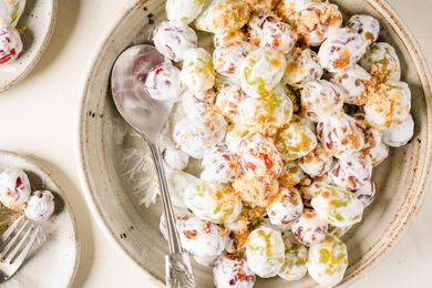 Bowl of grape salad with a spoon on the side topped with a creamy mixture and crumbled toppings