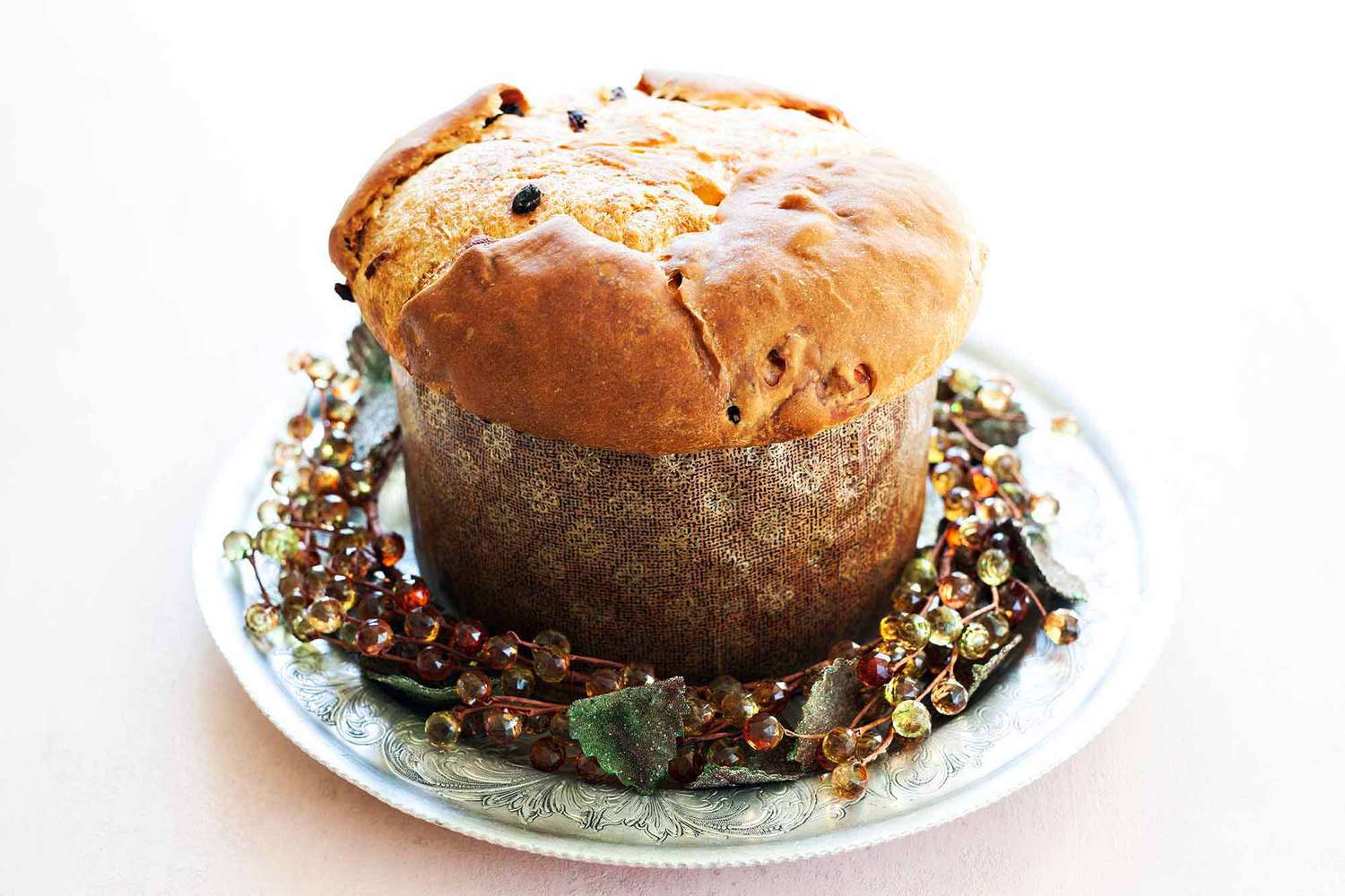 A loaf of homemade panettone in a paper mold with a holiday wreath around the base.