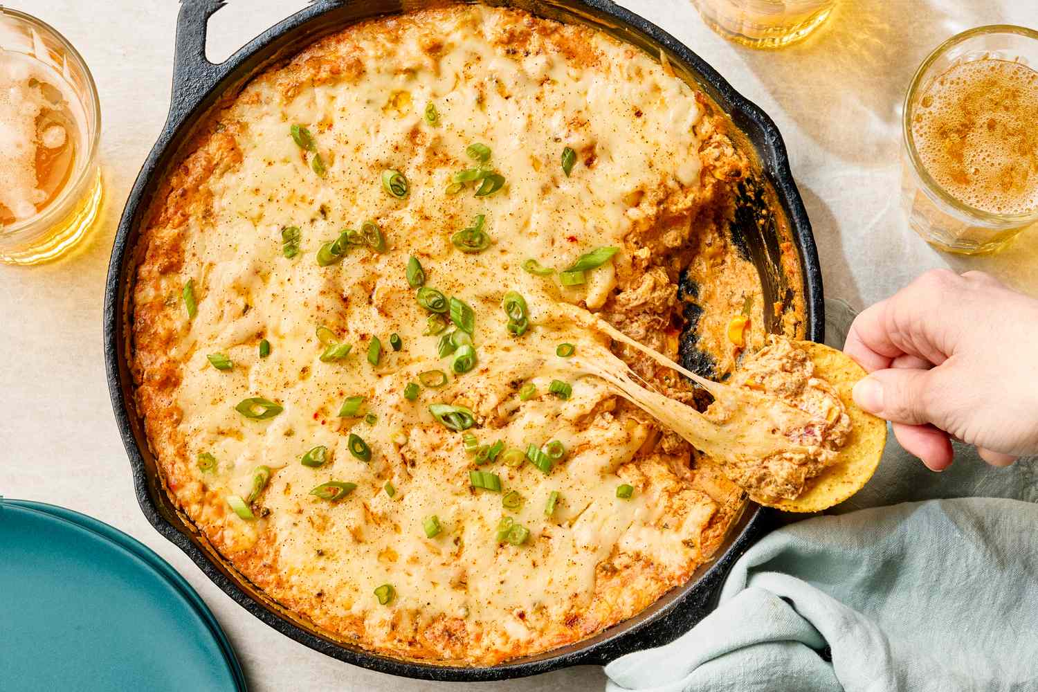 Hot dip in a castiron skillet someone scooping with a tortilla chip