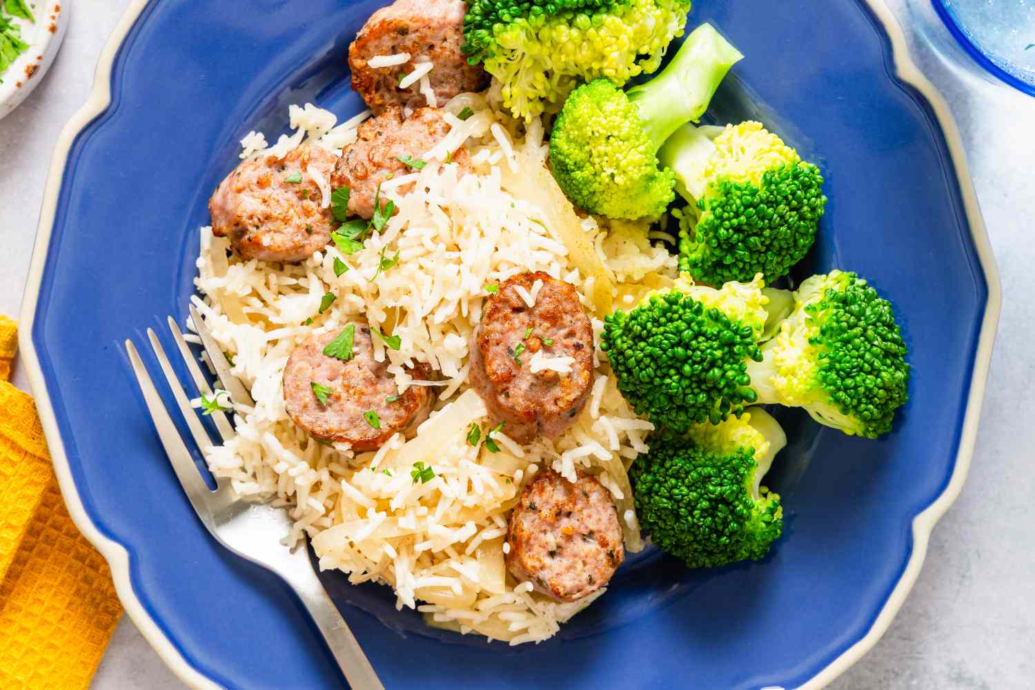 A plate with sliced sausage rice and broccoli floret sides