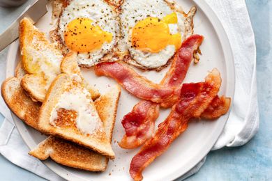 Cooked bacon on a plate with buttered toast and fried eggs
