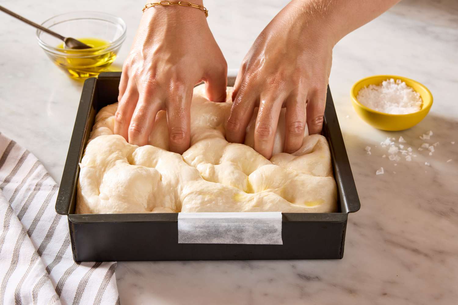 hands poking raw focaccia dough in pan for King Arthur Flour’s Big and Bubbly Focaccia