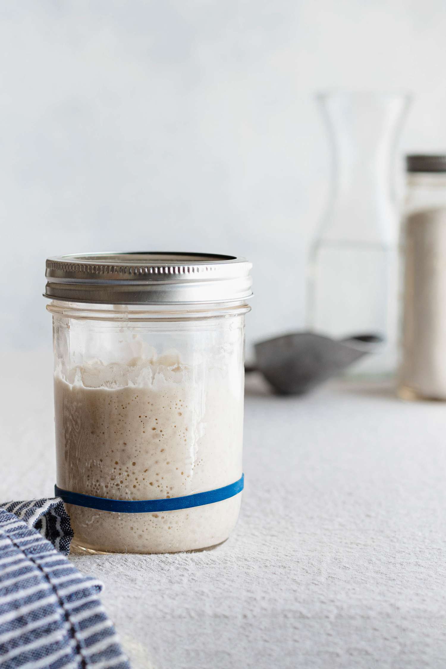 Side view of a mason jar with a rubberband around it and filled with a simple sourdough starter.