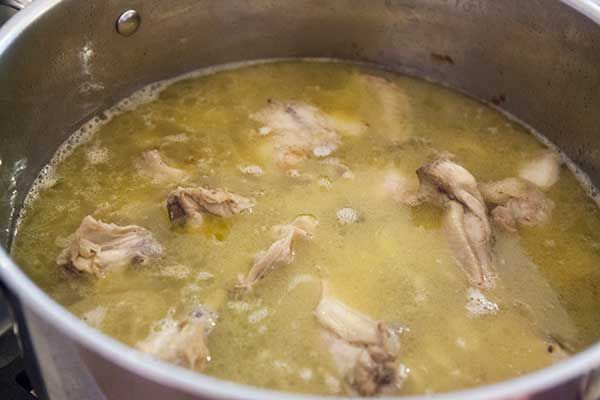 Chicken pieces, onions, and water simmering in a stock pot