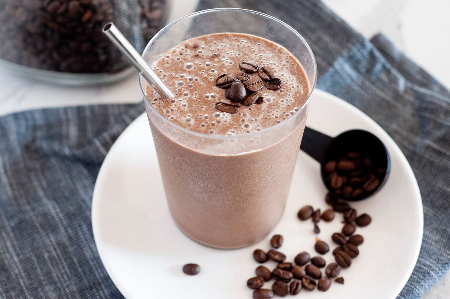 Creamy mocha coffee smoothie with a straw and set on a white plate with coffee beans next to it
