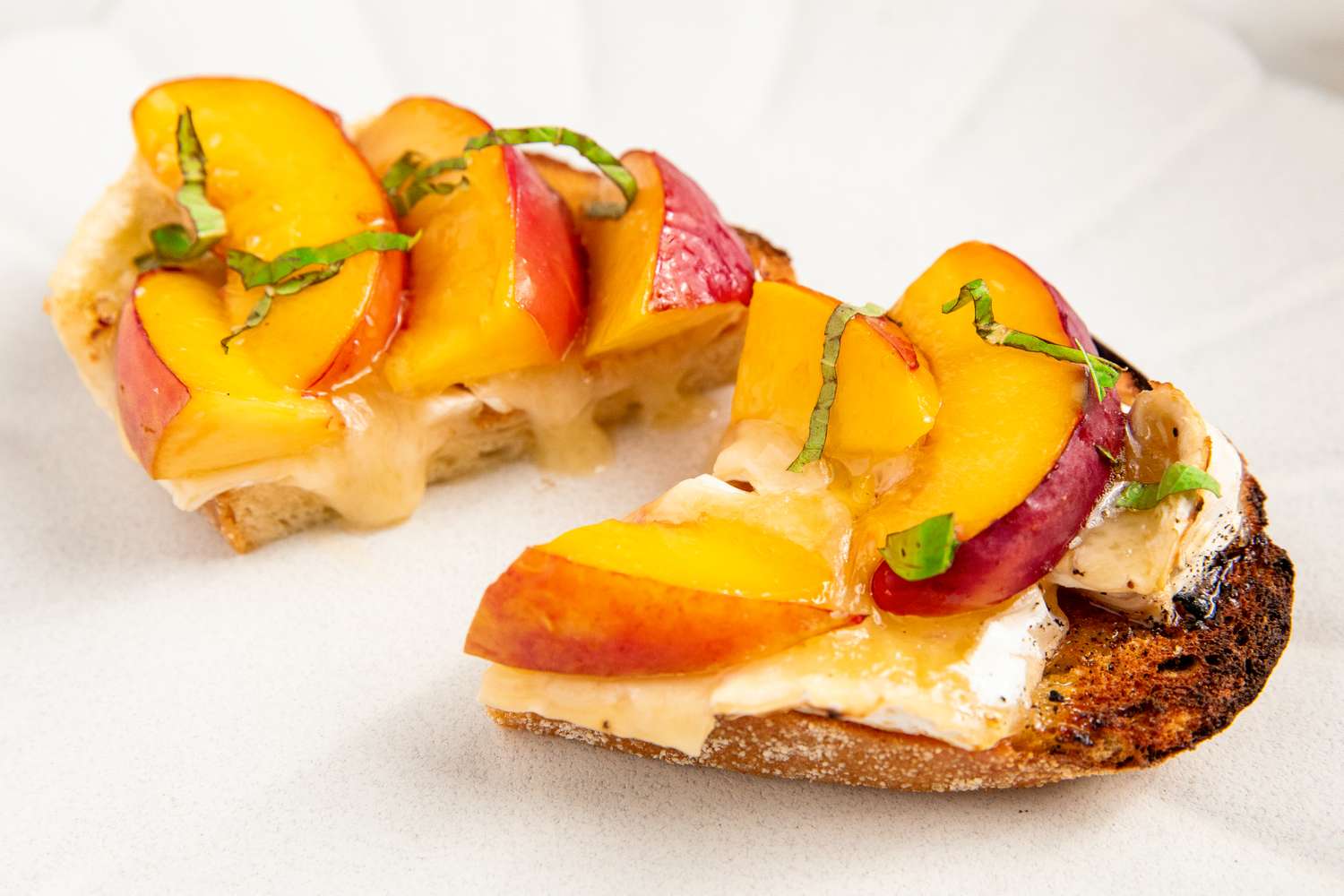 Two slices of toast topped with brie cheese nectarine slices and garnished with herbs