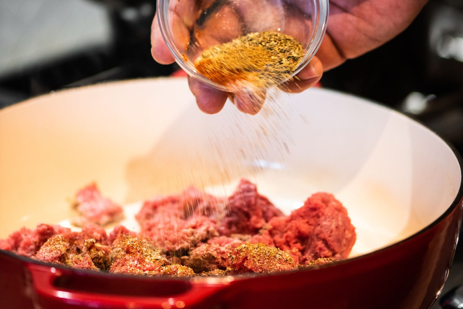 Bowl of Seasoning Added to Ground Beef in a Dutch Oven on a Stove for Cheeseburger Casserole Recipe