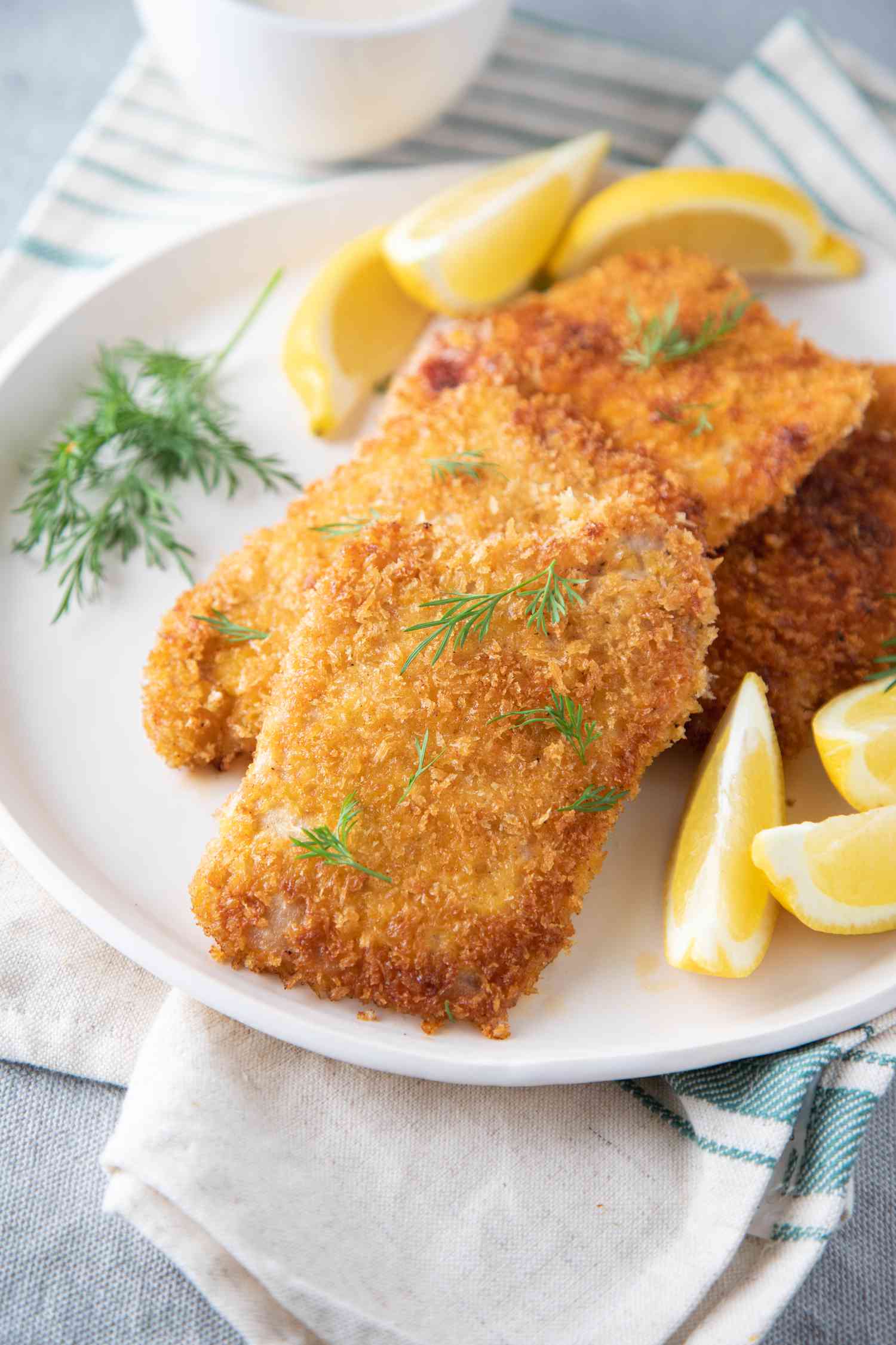 A plate of pork schnitzel on a white plate served with lemons and dill.