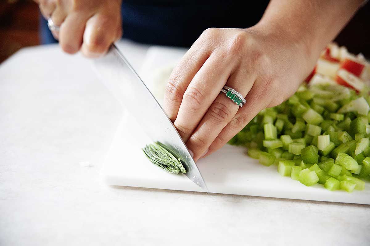Woman chopping sage leaves on a white cutting board.