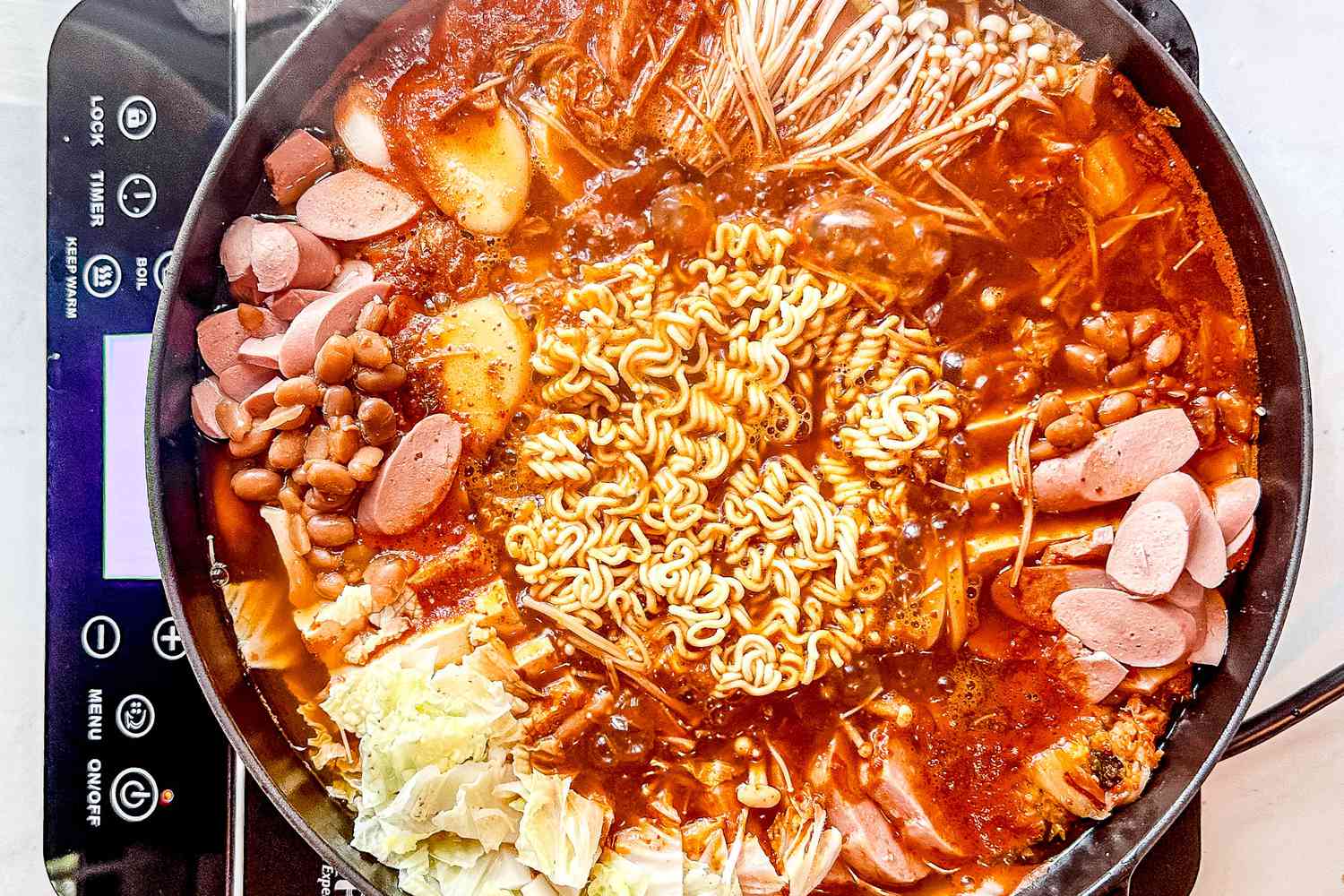 Pot of budae jjigae (army based stew) cooking in a pot over a portable induction stove