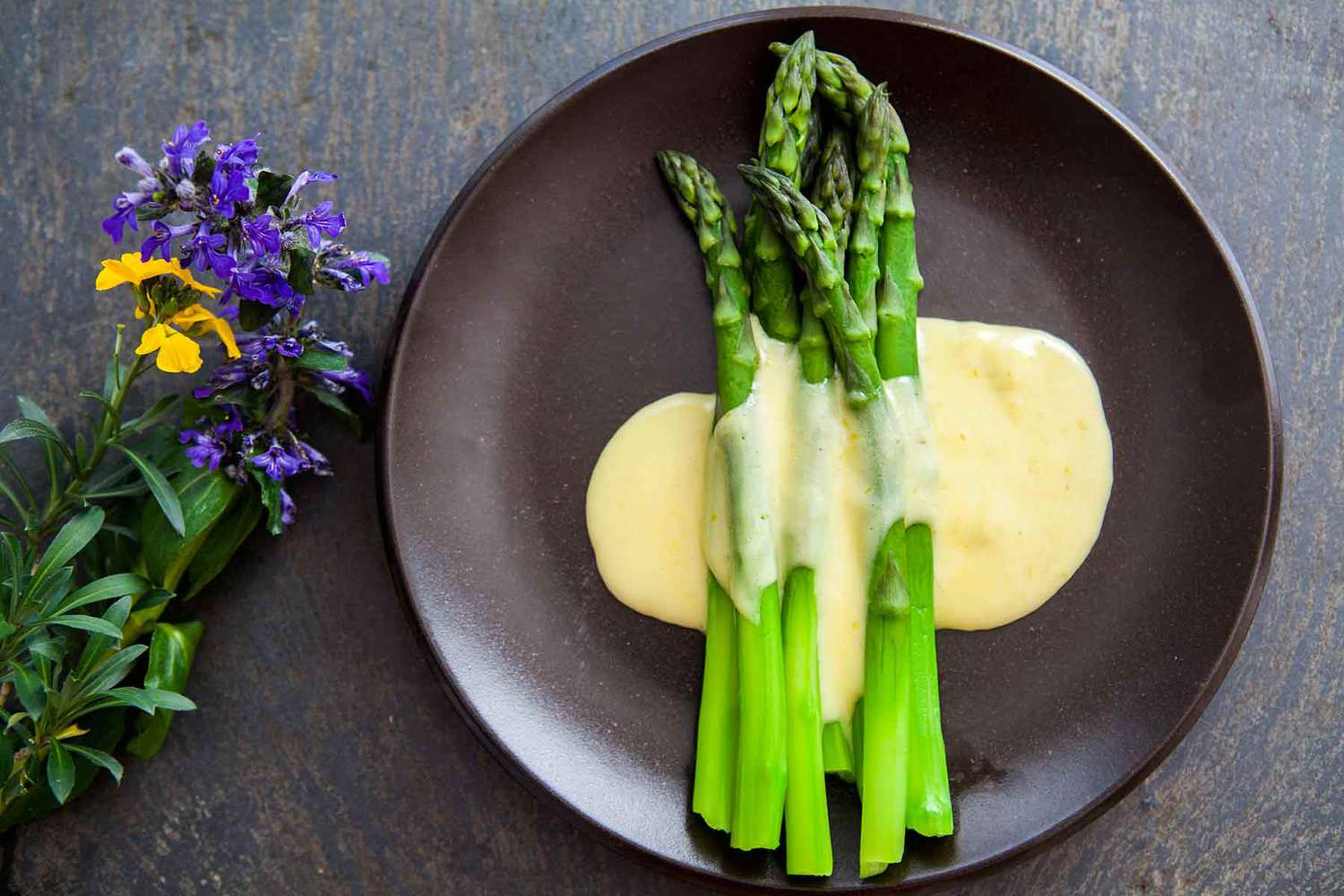Steamed asparagus on a dark plate topped with Hollandaise sauce