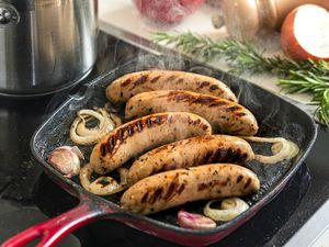 Sausages grilling in a pan with onions and garlic