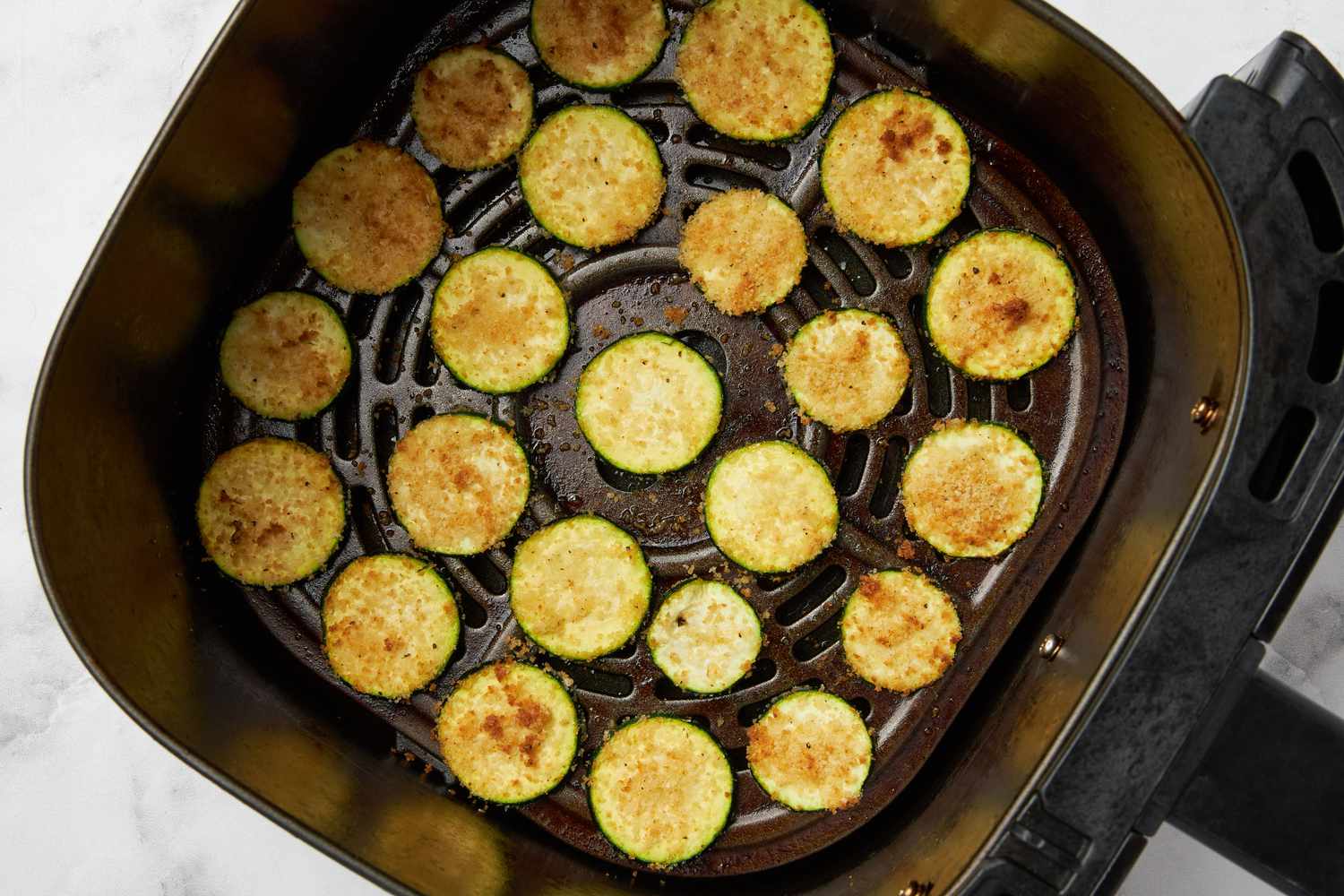 Zucchini slices partially cooked in an air fryer basket