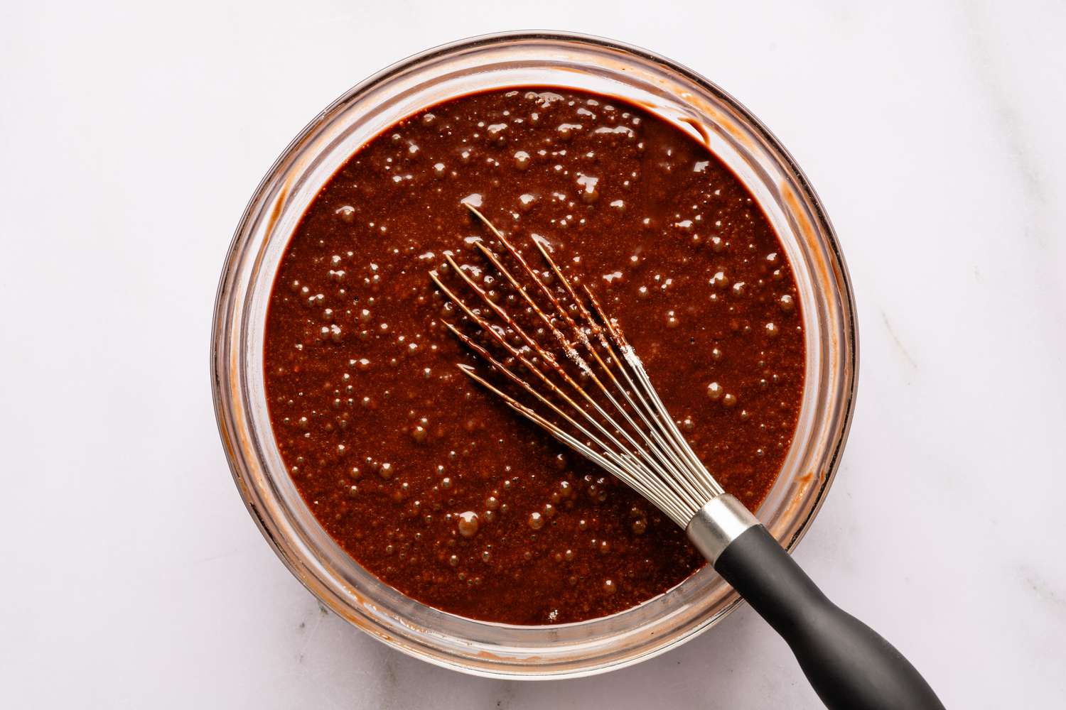 Overhead view of a clear glass bowl and whisk with the batter after whisking all ingredients together for Easy Brooklyn Blackout Cake recipe